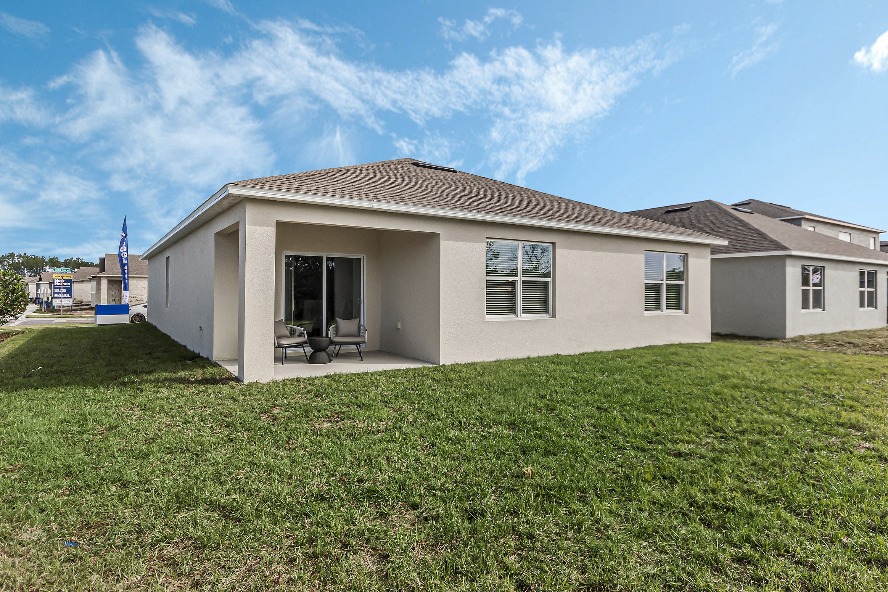 Charming single-story home featuring a cozy patio with seating, surrounded by lush green grass, under a clear blue sky.