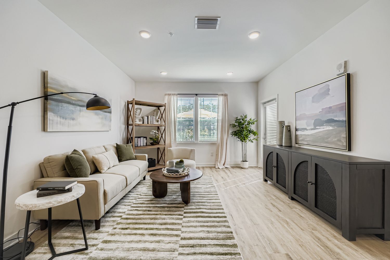 Bright and modern living room featuring a cozy beige sofa, stylish artwork, and abundant natural light from large windows.