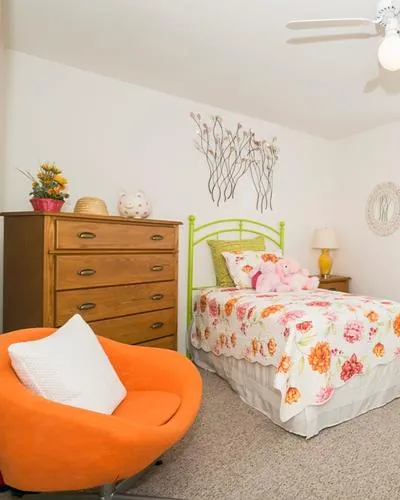 Charming bedroom with floral bedding, vibrant orange chair, and cozy lighting, perfect for relaxation.