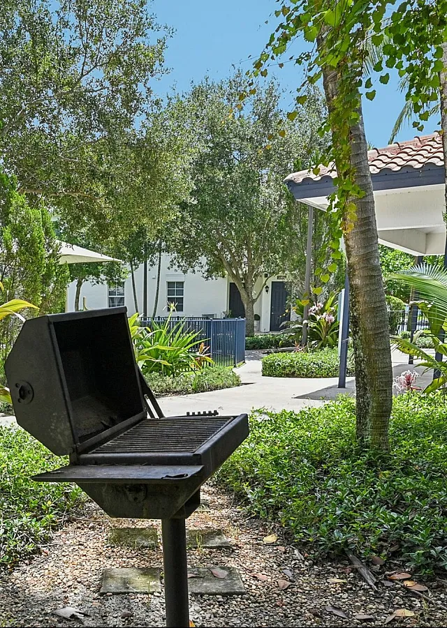 Charming outdoor area with lush greenery, featuring a barbecue grill and covered seating, perfect for relaxation and entertaining.