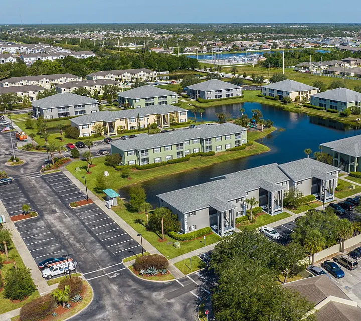 Aerial view of a serene apartment complex with lush green surroundings, multiple buildings, and a tranquil central pond.