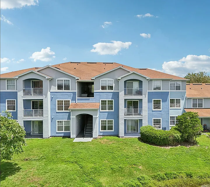 Charming apartment building with vibrant blue facade, surrounded by lush greenery and warm natural sunlight.