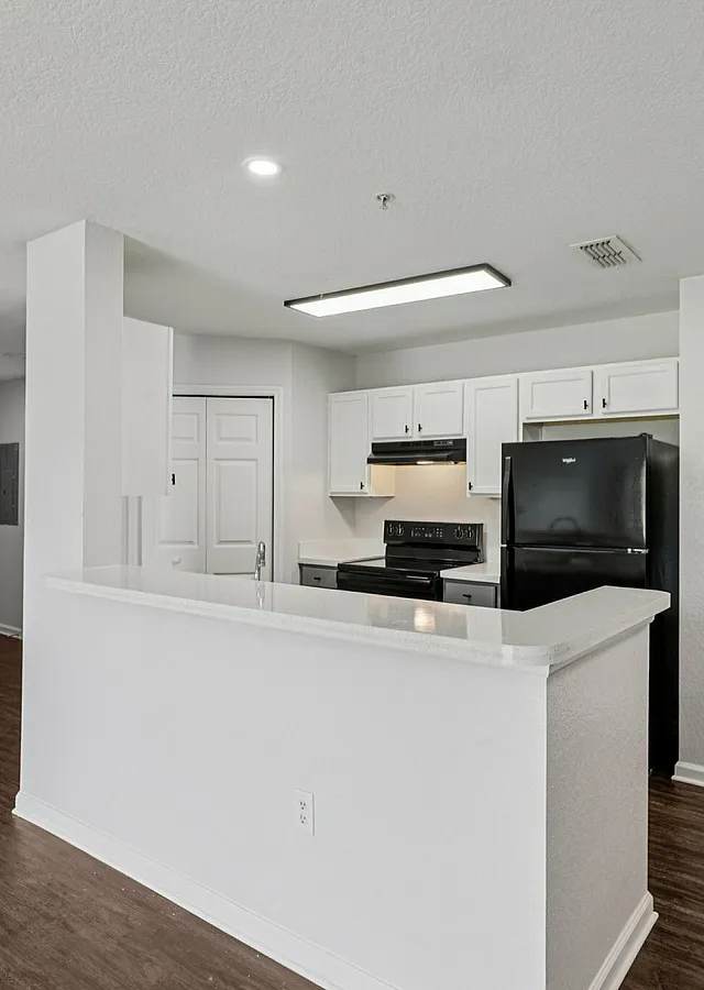 Modern apartment kitchen with sleek white cabinets, black appliances, and a stylish breakfast bar accentuated by elegant wood flooring.