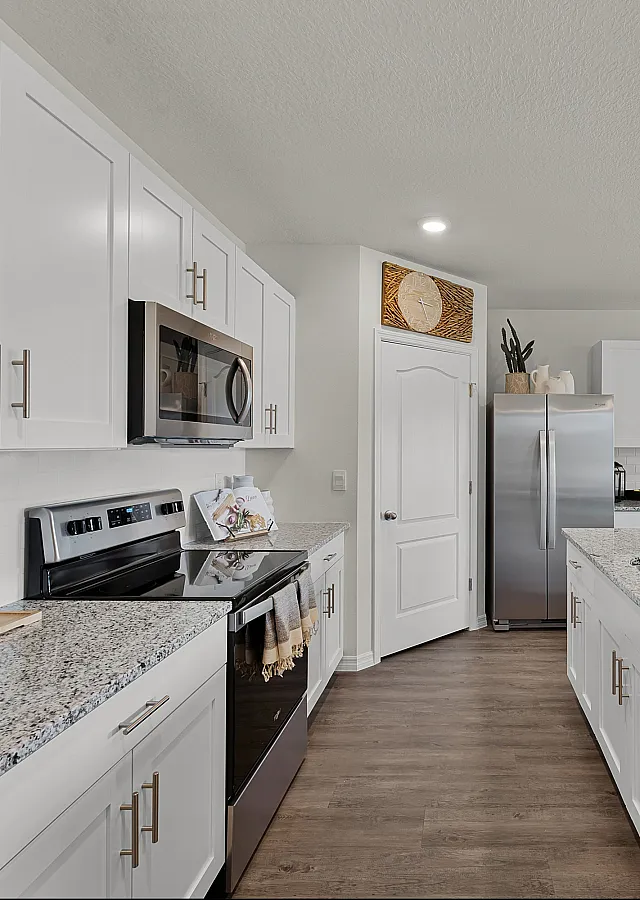 Modern kitchen featuring sleek white cabinets, stainless steel appliances, and elegant granite countertops, seamlessly leading to a bright dining area.