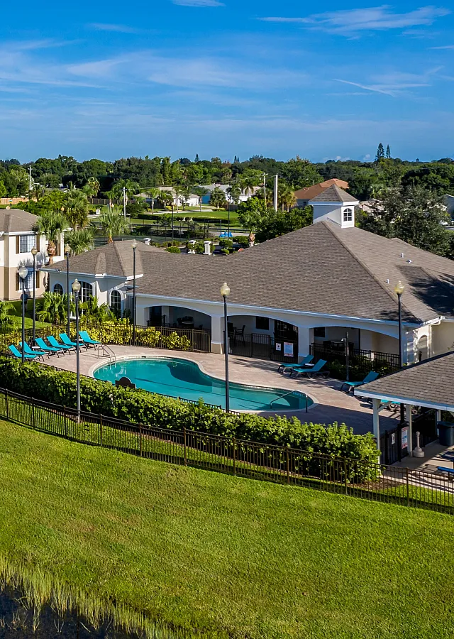 Charming apartment complex with lush green lawns, a shimmering pool, and peaceful water views, perfect for relaxation and community living.