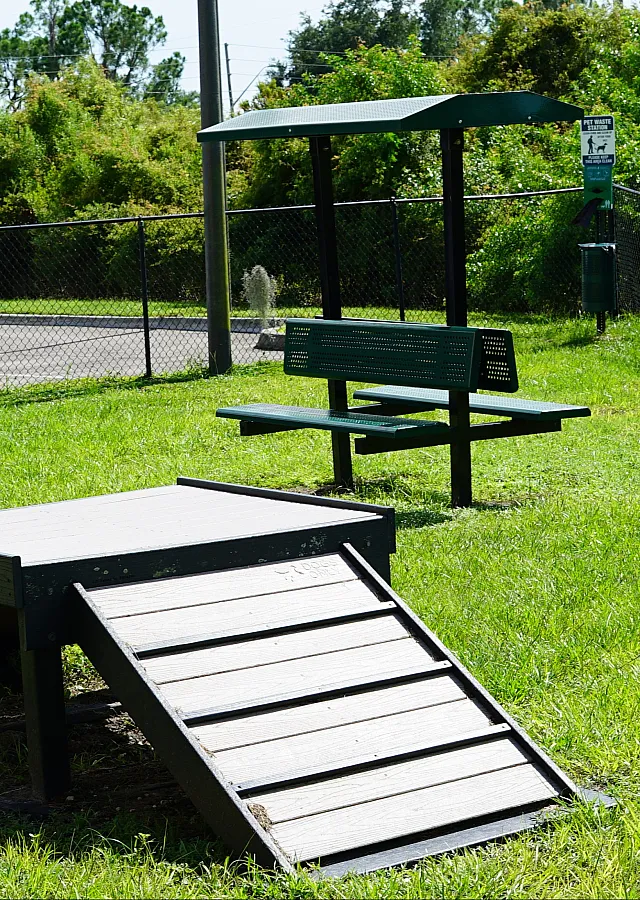 Inviting dog park with a shaded seating area, agility ramp, and lush greenery, perfect for pet-friendly living.