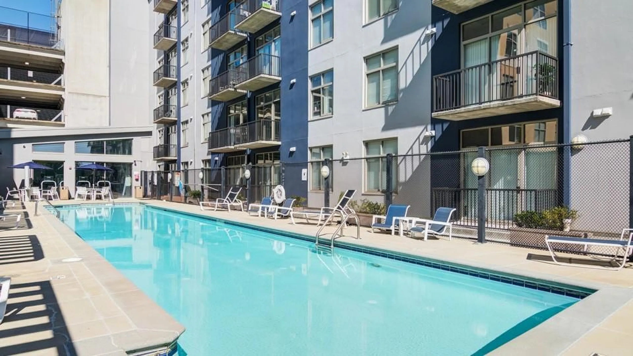 Luxurious apartment complex with a sparkling outdoor pool, modern lounge chairs, and contemporary building design.