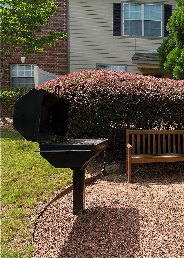 Charming outdoor space with a cozy wooden bench, classic barbecue grill, and lush greenery in a serene garden setting.