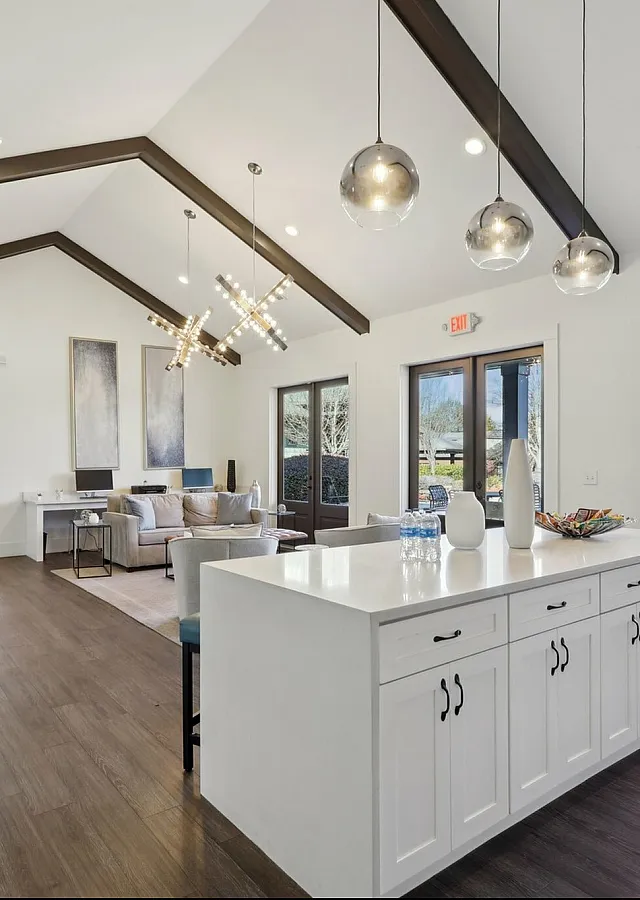 Luxurious open-concept living area with vaulted ceilings, modern lighting, and expansive views of a serene poolside through large glass doors.