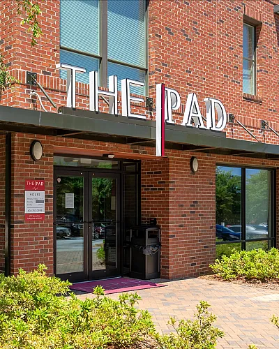 Charming modern apartment entry with brick fa&ccedil;ade and lush landscaping at The Pad, welcoming ambiance with natural light.