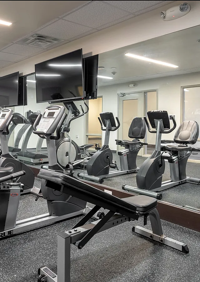 Modern fitness center equipped with state-of-the-art exercise bikes and treadmills, featuring large mirrors and mounted TVs.