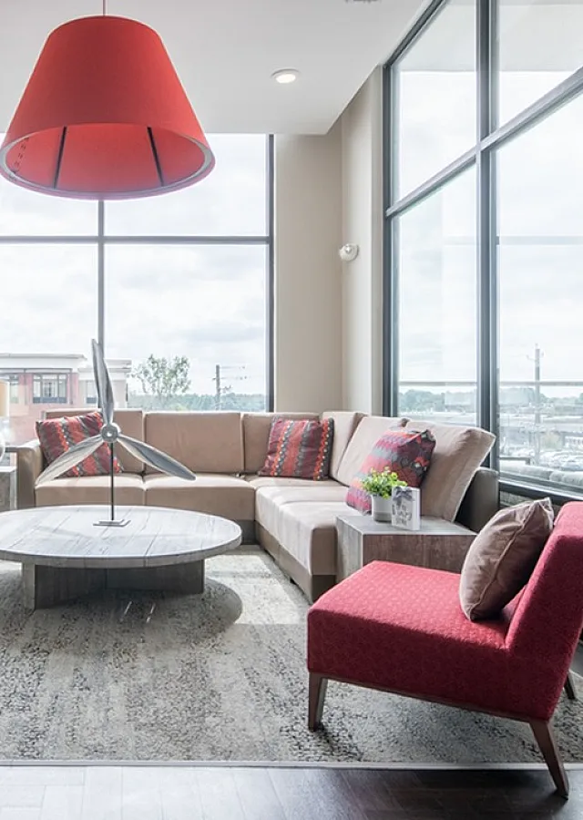Bright and modern living room with large windows, stylish sectional sofa, and bold red accents.
