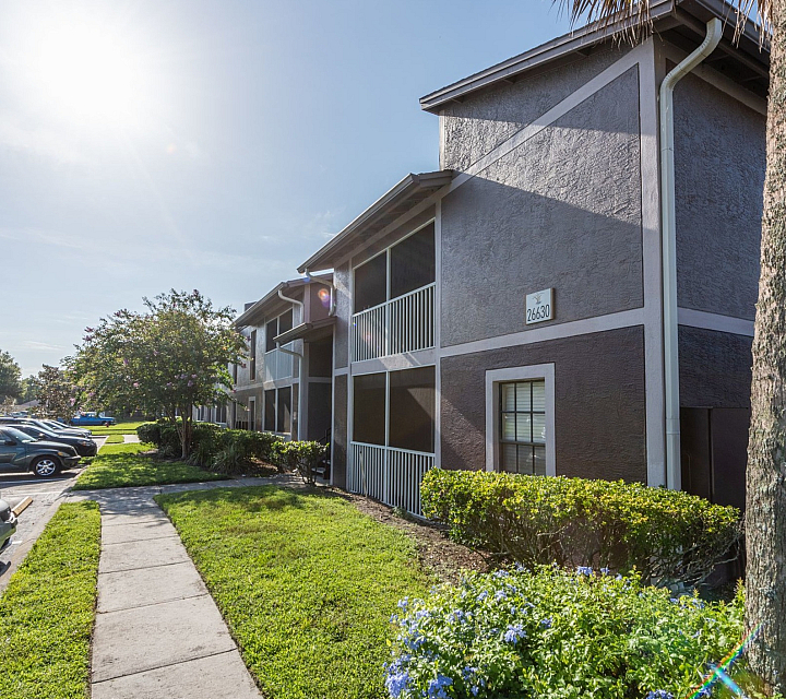 Charming apartment exterior with lush landscaping, vibrant blue flowers, and sunlit balconies for peaceful living.