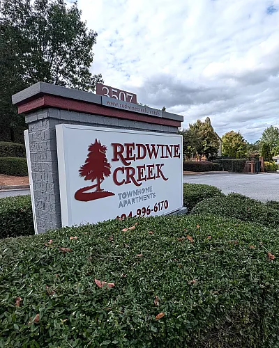 Inviting signage for Redwine Creek Townhome Apartments surrounded by lush greenery under a bright blue sky.