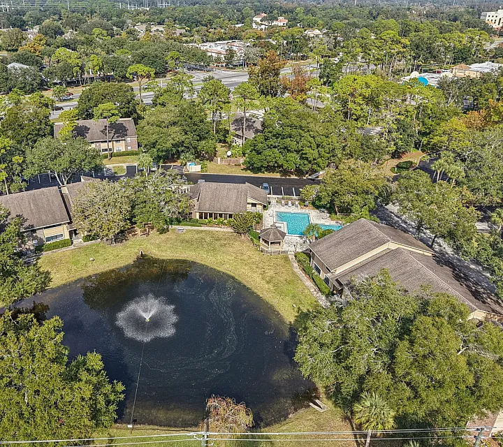Scenic aerial view of tranquil residential community with lush greenery, serene pond, and refreshing swimming pool.