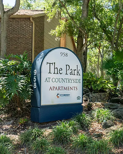 Inviting entrance to The Park at Countryside Apartments surrounded by lush greenery and mature trees, creating a serene living environment.