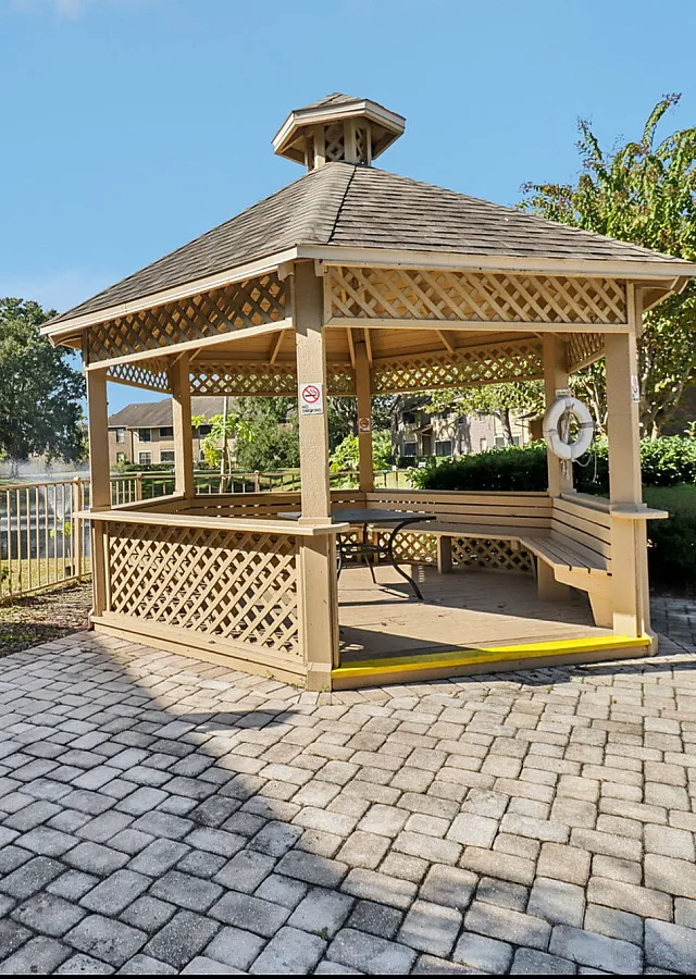 Charming outdoor gazebo with seating, nestled by a serene pond and lush landscaping, perfect for relaxation and gatherings.