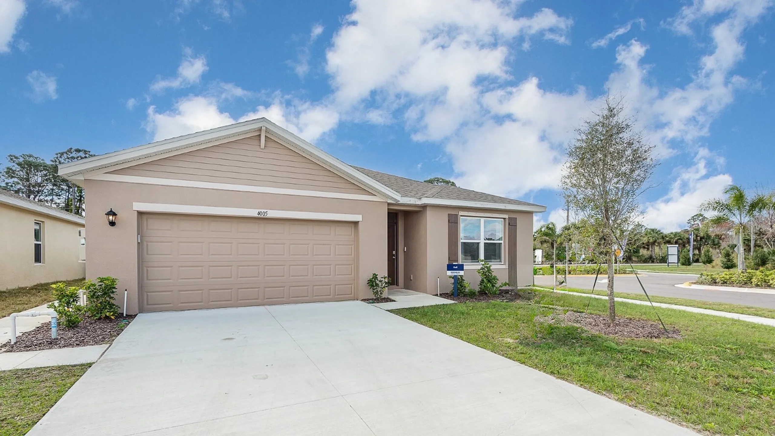 Charming single-story home with a spacious two-car garage, surrounded by lush greenery under a clear blue sky.