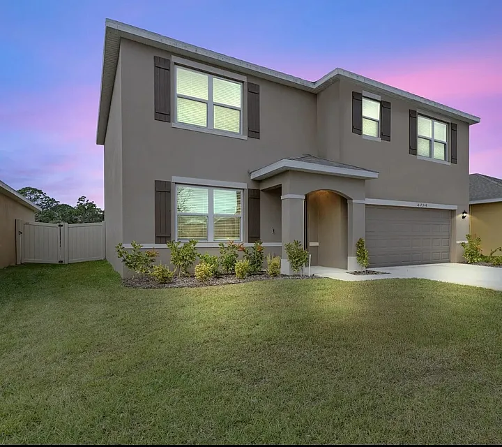 Charming two-story home with manicured lawn against a stunning pink and blue sunset sky, ideal for peaceful suburban living.