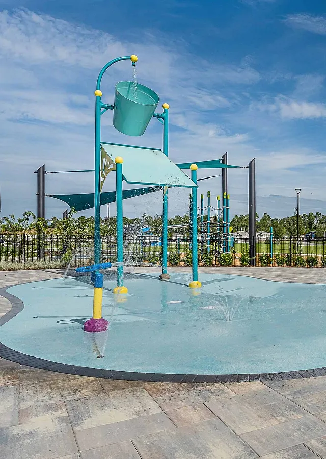 Vibrant outdoor splash pad with playful water features and bright-colored structures set against a clear blue sky.