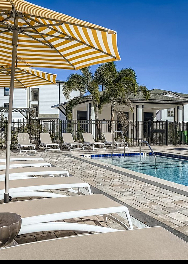 Inviting outdoor pool area with stylish lounge chairs, vibrant yellow umbrellas, and lush palm trees creating a tropical retreat.