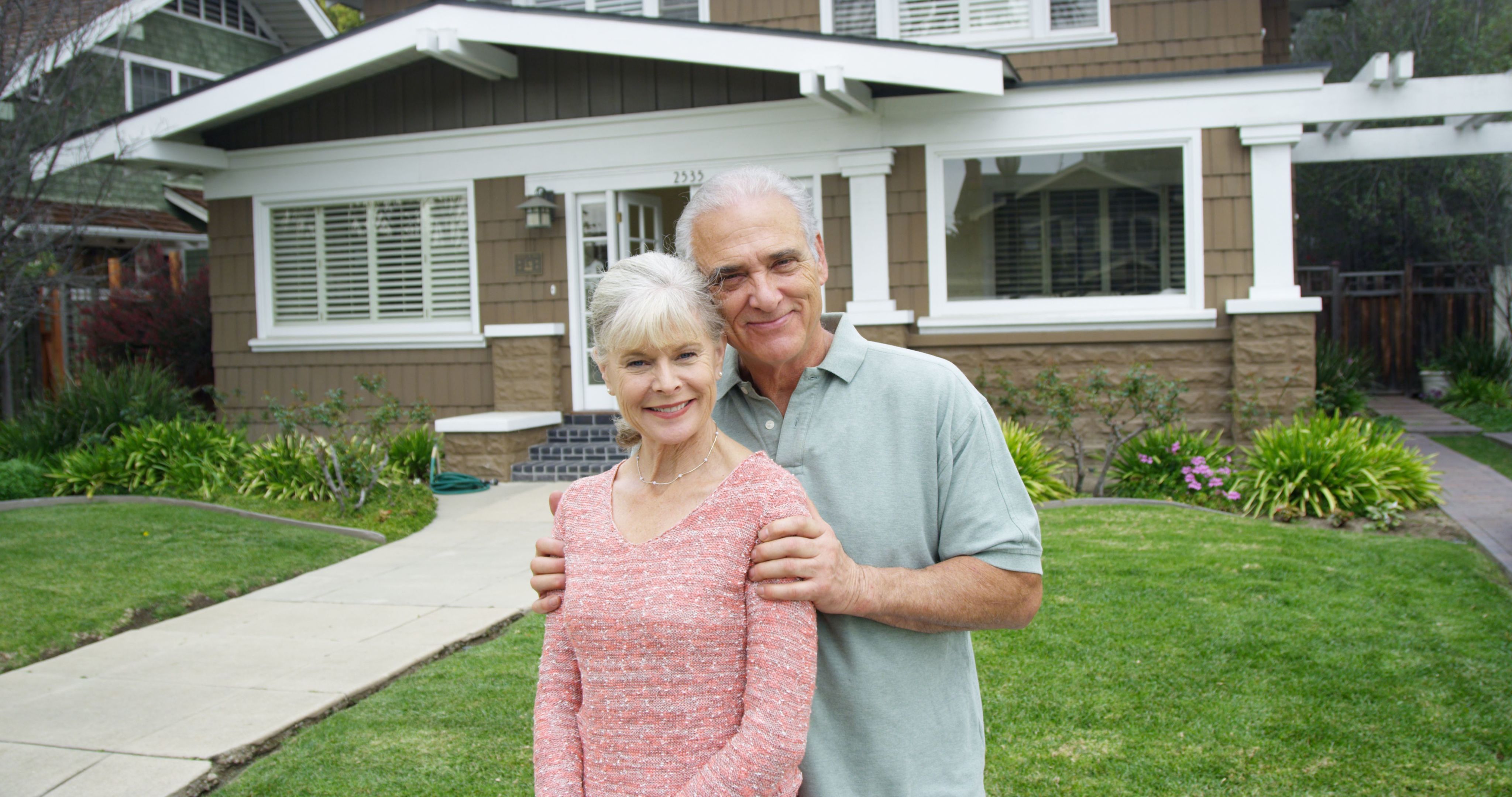 Happy senior couple standing in front of their home