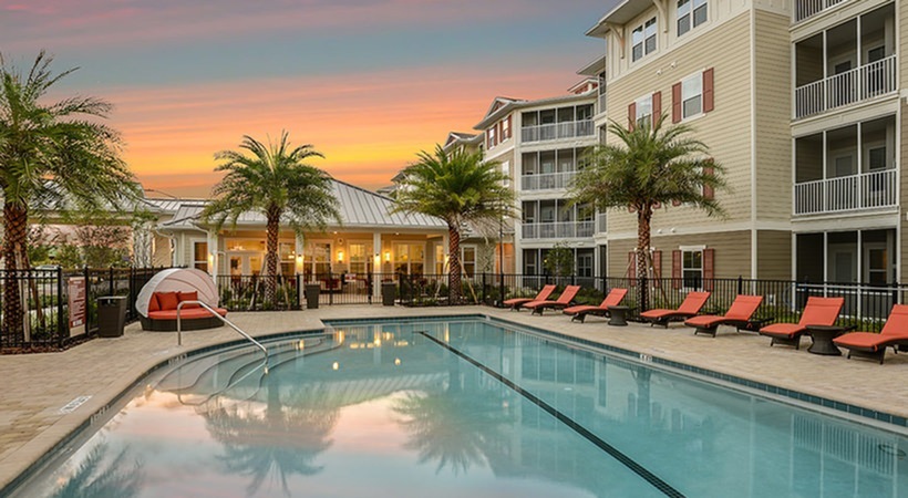 Monterey Pointe, exterior, sparkling blue swimming pool, orange lounge chairs, building exterior, four levels, balconies, red shudders,