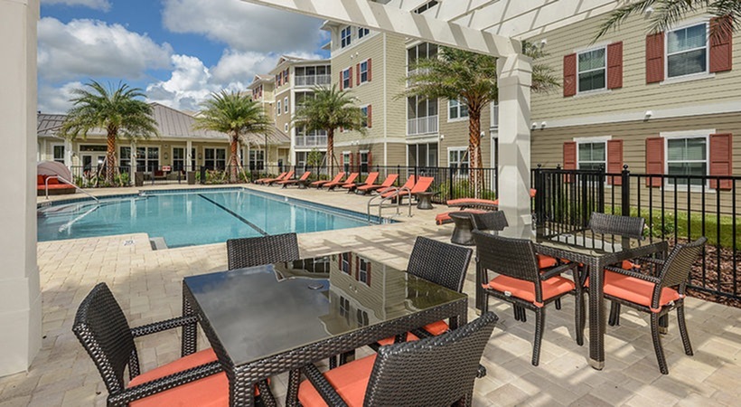 Monterey Pointe, exterior, pergola seating, black tables, black and orange chairs, adjacent to pool, building exteriors, red shudders, clubhouse, balconies
