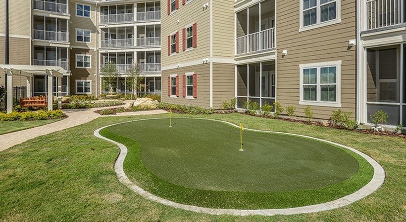 Monterey Pointe, exterior, putting green, courtyard, landscaping, walkways, tan and brown buildings, four levels, balconies, red shudders, pergola seating