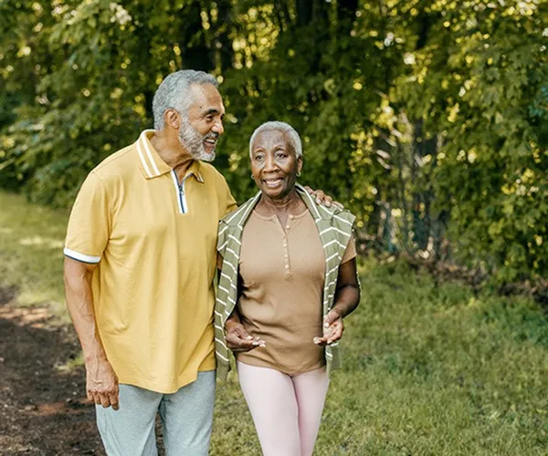 Two people walking together outdoors near Elate Rancho Cucamonga Apartments in Rancho Cucamonga, CA, featuring sunlit trees.