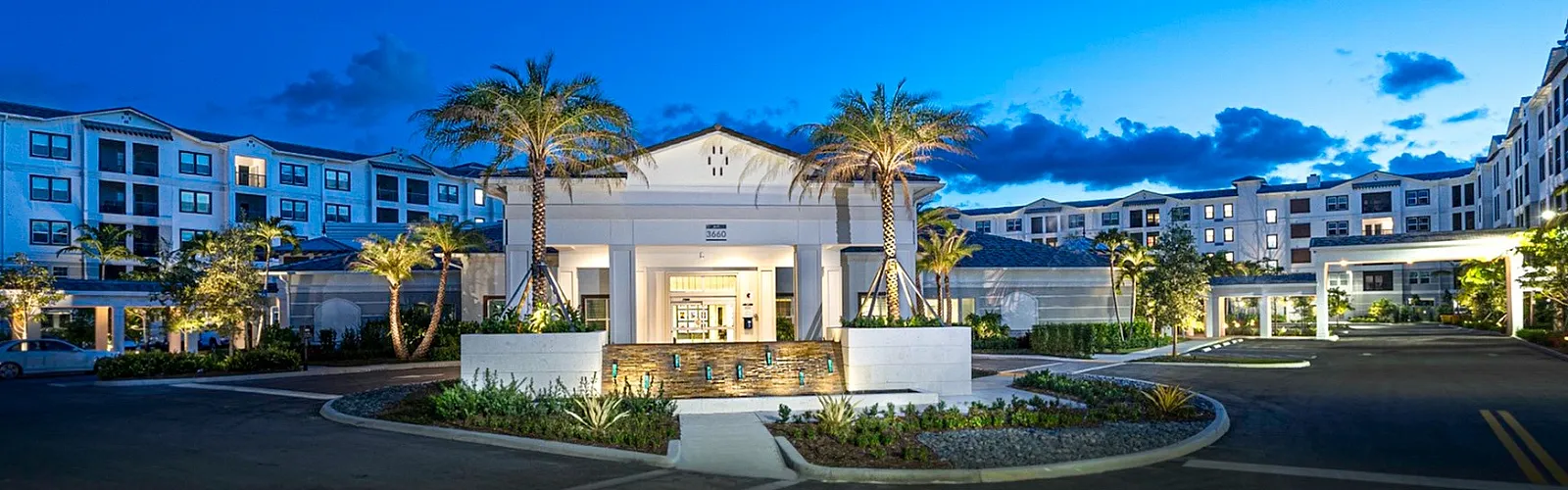 Luxurious apartment complex entrance illuminated at dusk with palm trees and elegant architecture inviting you to a serene oasis.