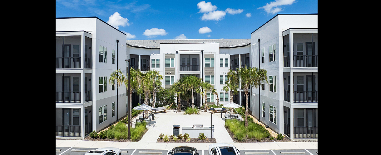 Elegant apartment complex with modern design featuring lush landscaped courtyard, palm trees, and inviting outdoor seating areas under a clear blue sky.