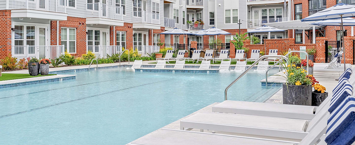 Chic apartment complex featuring a luxurious swimming pool with stylish lounge chairs and vibrant landscaping, perfect for relaxation and sunny days.