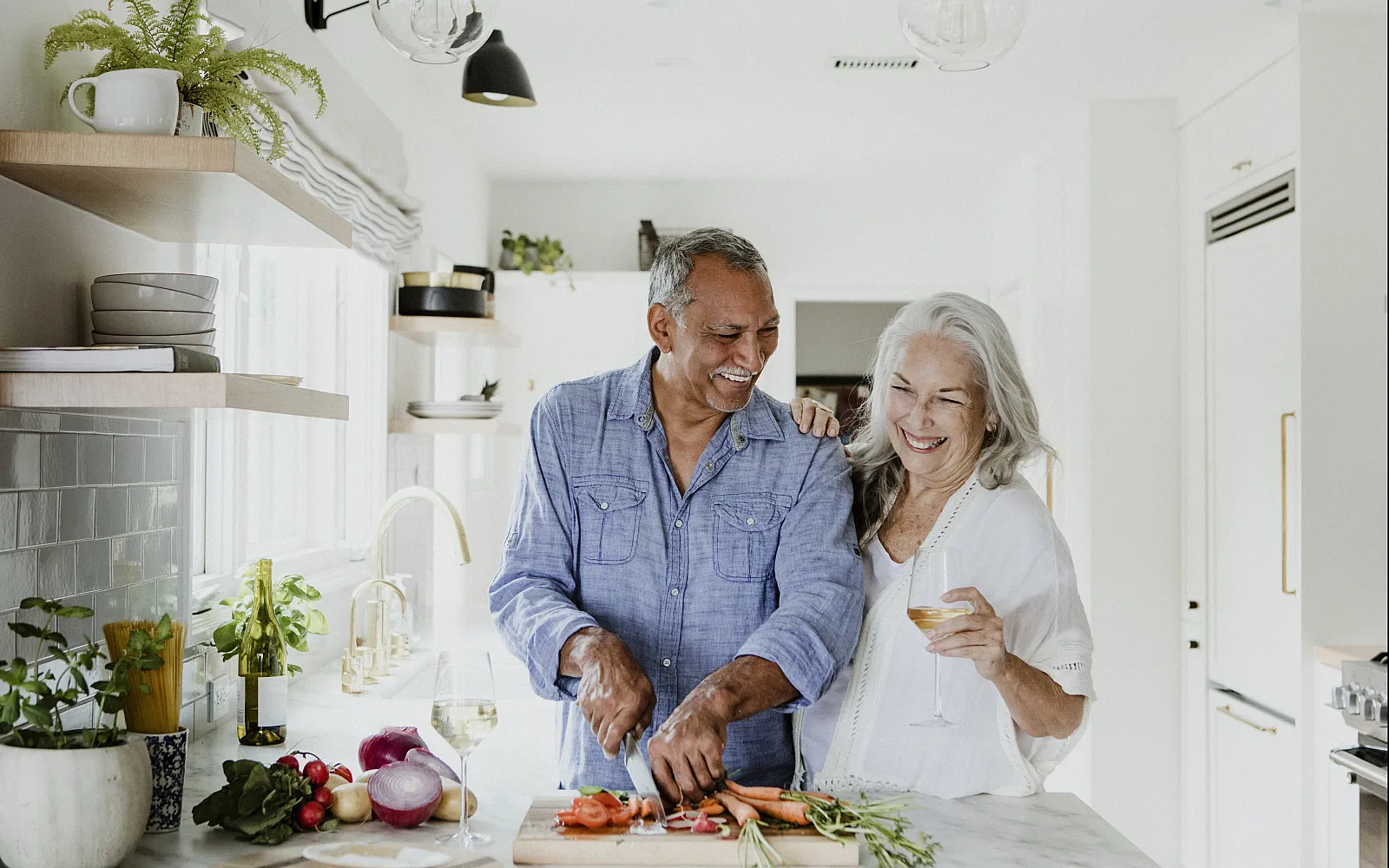 Bright and airy kitchen with elegant fixtures, featuring a couple enjoying cooking together surrounded by fresh vegetables and wine, highlighting a warm and inviting atmosphere.
