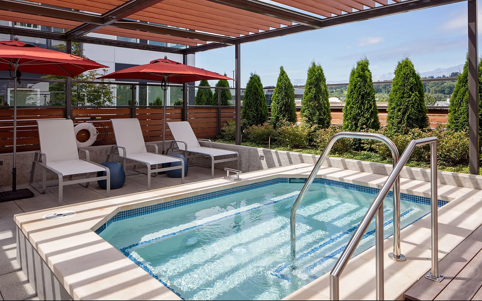 Luxurious outdoor pool area with sleek lounge chairs and vibrant red umbrellas, encased by lush greenery for a serene retreat.