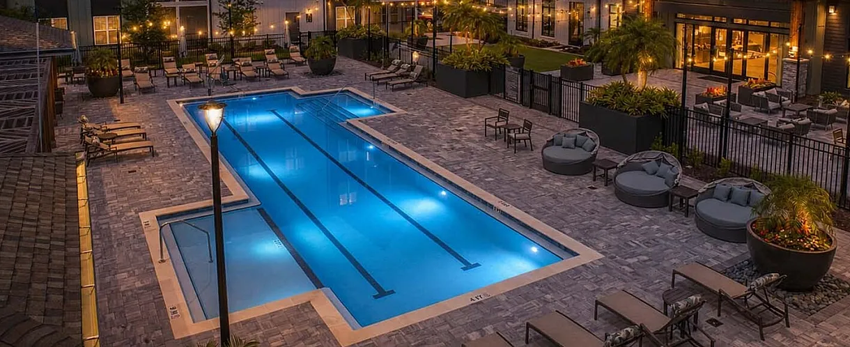 Charming apartment complex with a glowing pool and inviting lounge area under a vibrant sunset sky.