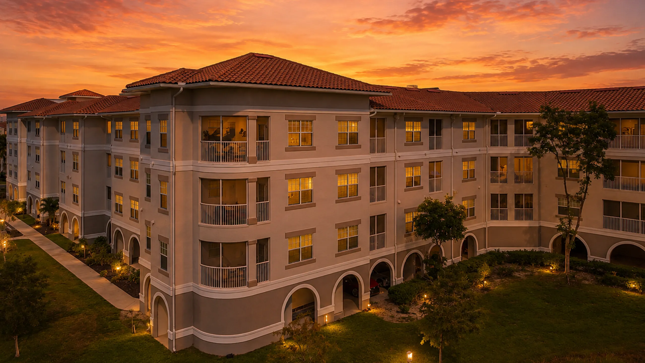 Charming multi-story apartment building with Mediterranean-style architecture, featuring elegant balconies and lush landscaped surroundings under a clear blue sky.