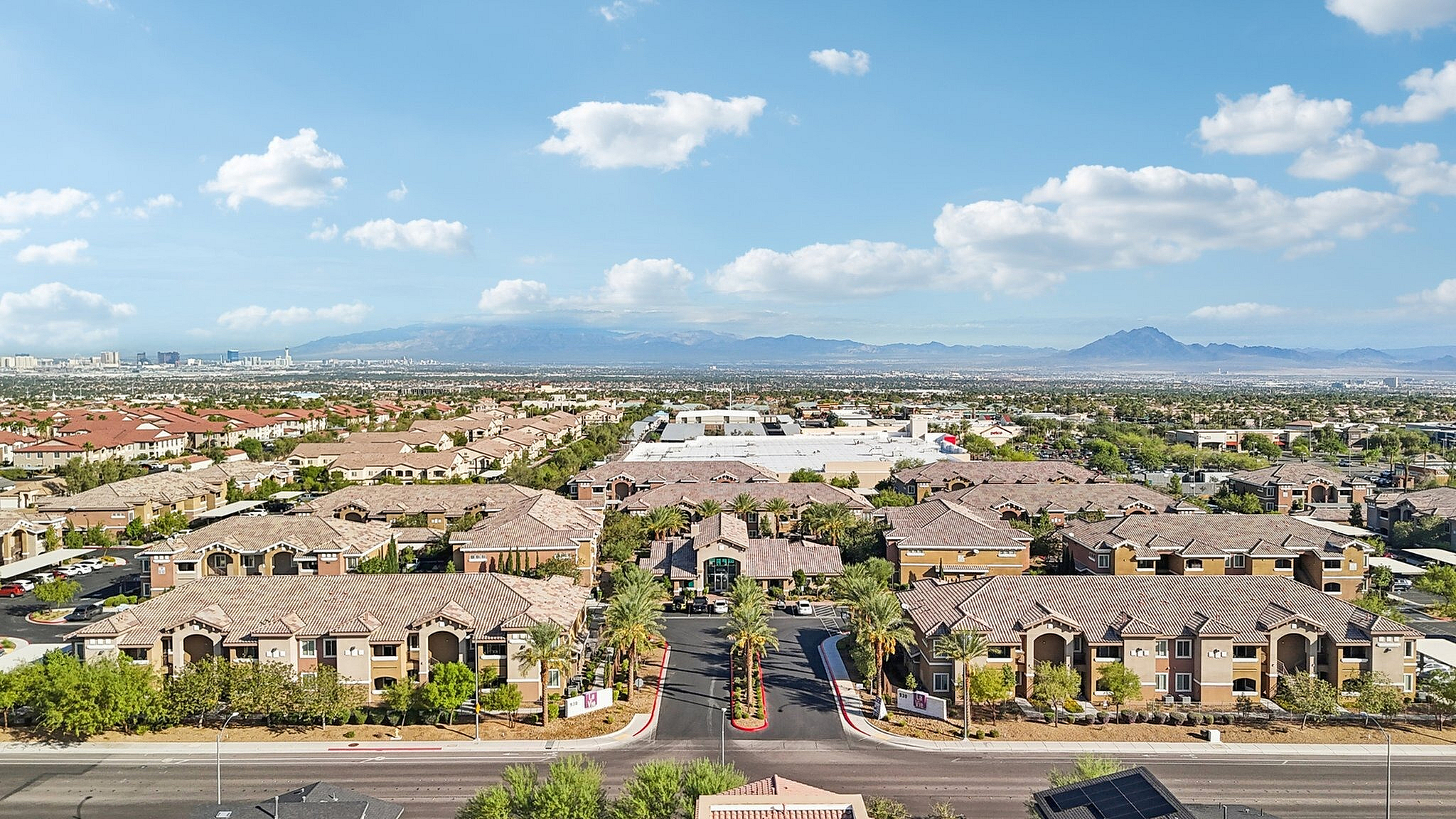 Breathtaking aerial view of a sprawling residential community with tiled roofs and lush greenery, set against a backdrop of distant mountains under a clear blue sky.