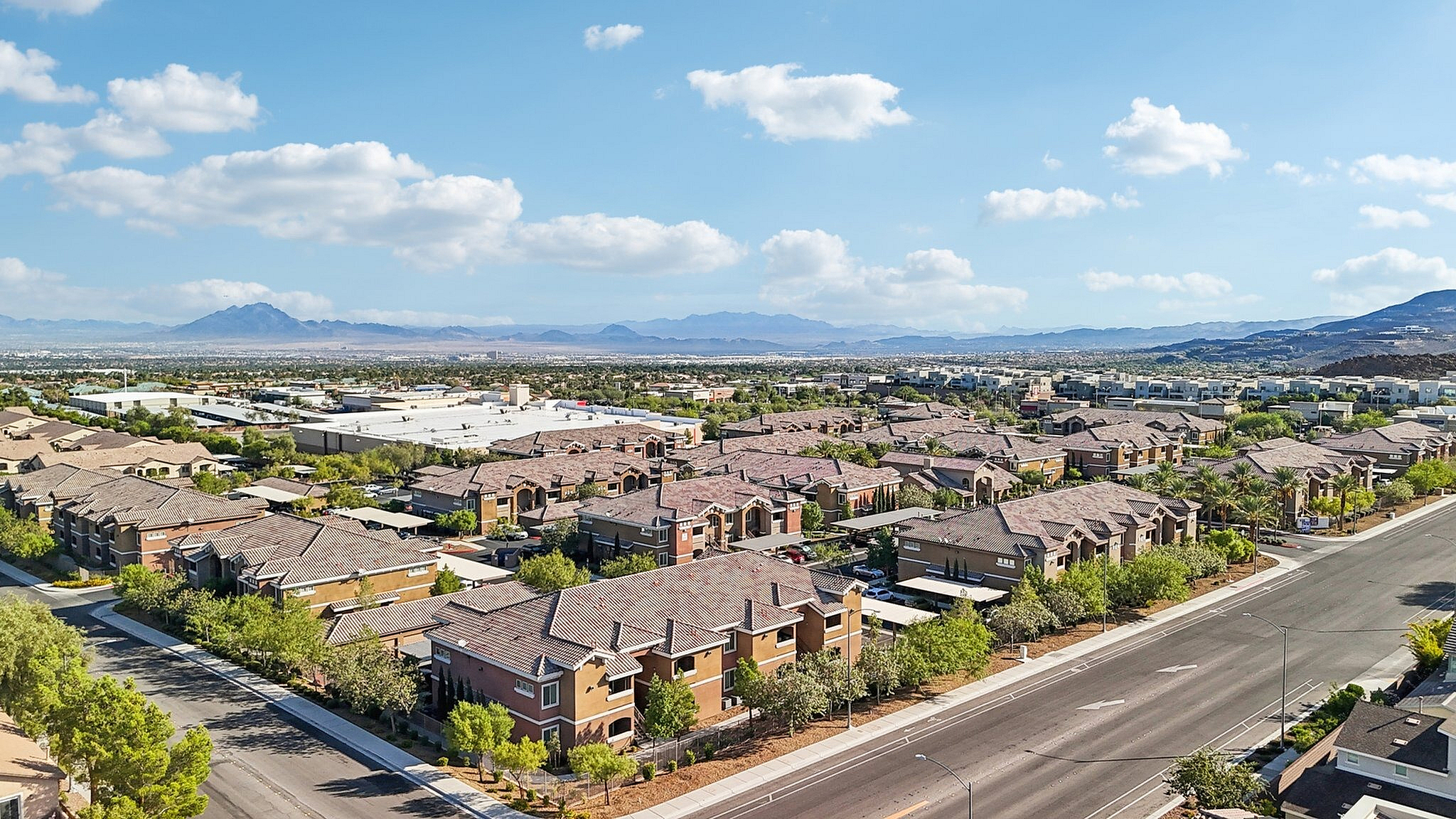Stunning aerial view of a modern apartment complex surrounded by lush greenery and scenic mountains, offering an ideal living environment.