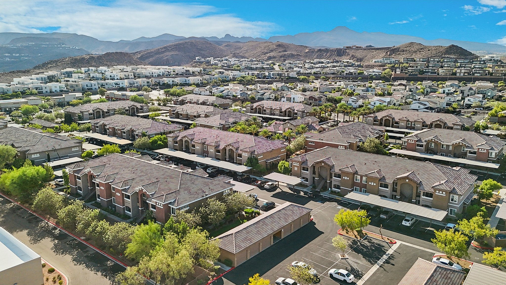 Stunning aerial view of a modern residential community nestled among picturesque hills, showcasing stylish apartment buildings, lush greenery, and vibrant cityscape.