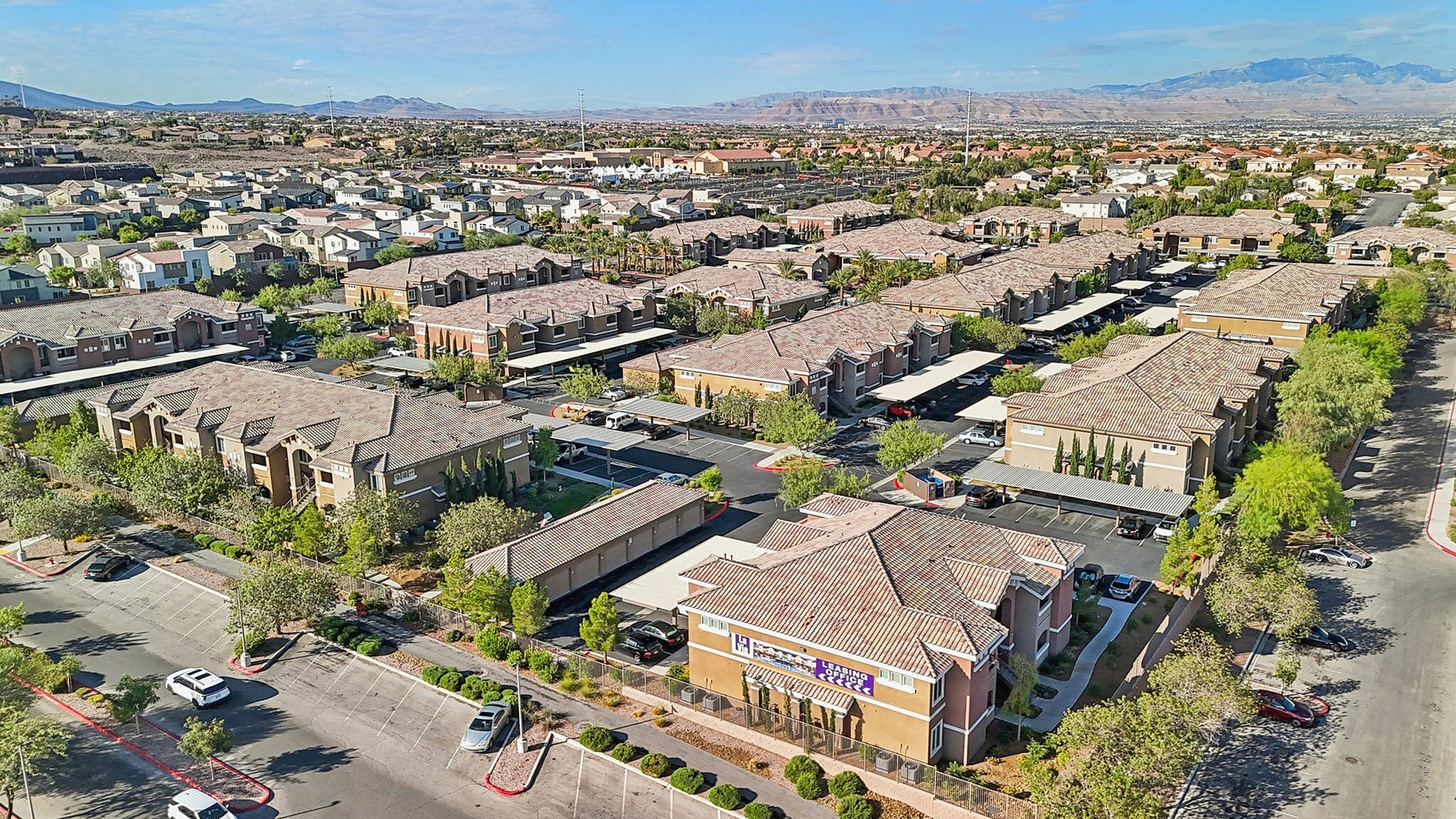 Scenic aerial view of a charming residential community with modern apartments, lush greenery, and distant mountain backdrop, offering serene living.