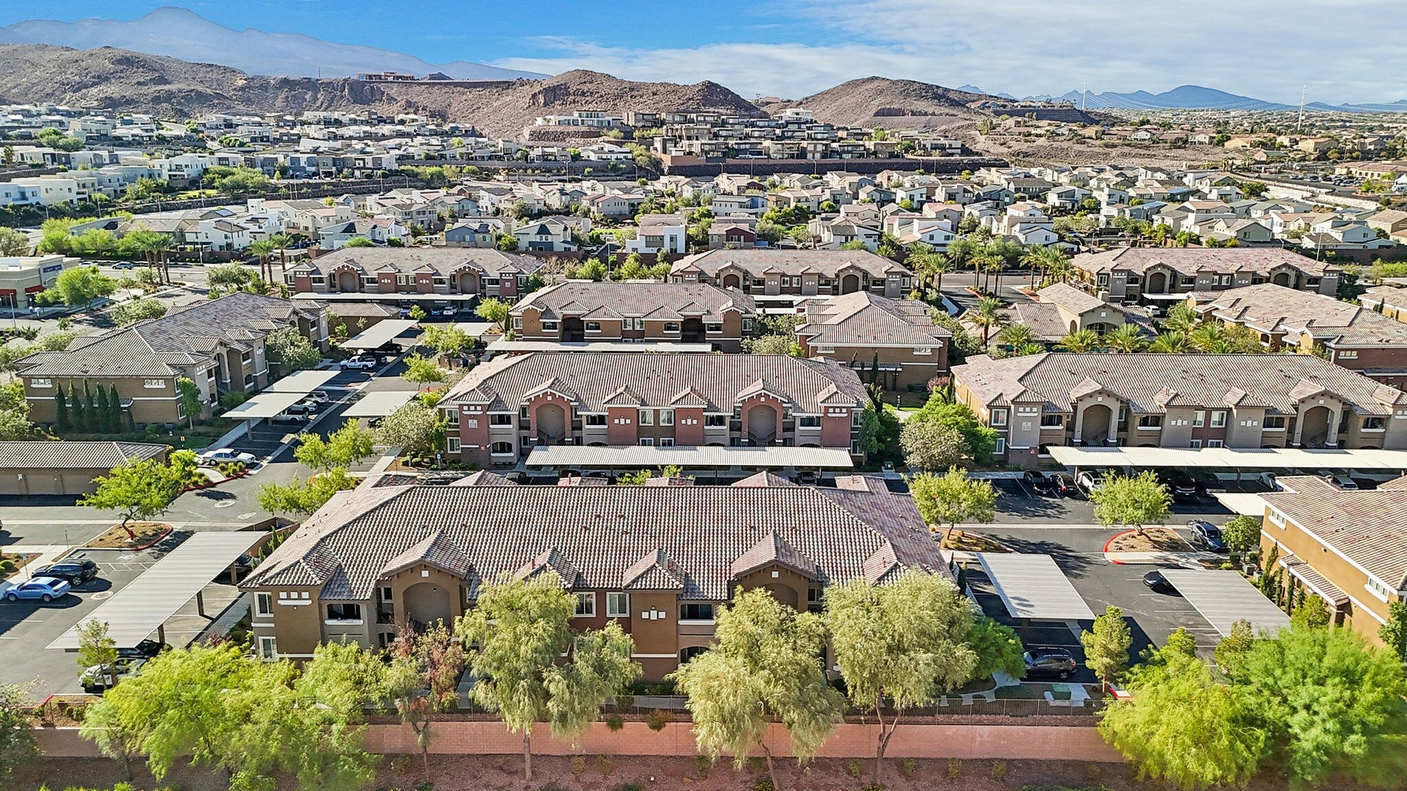 Vibrant aerial view of a picturesque residential community nestled amidst scenic hills, showcasing well-maintained apartment buildings and lush green landscapes.