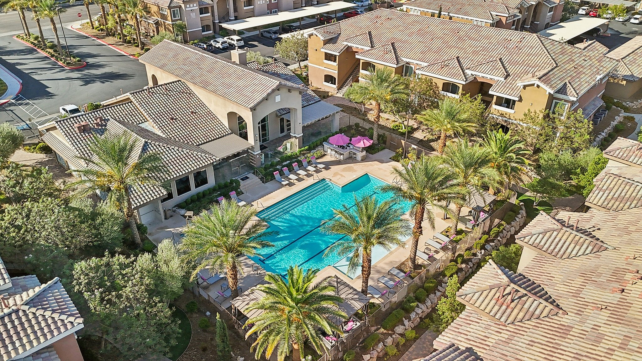 Luxurious aerial view of a modern apartment complex featuring a sparkling pool, elegant palm trees, and inviting sun loungers.