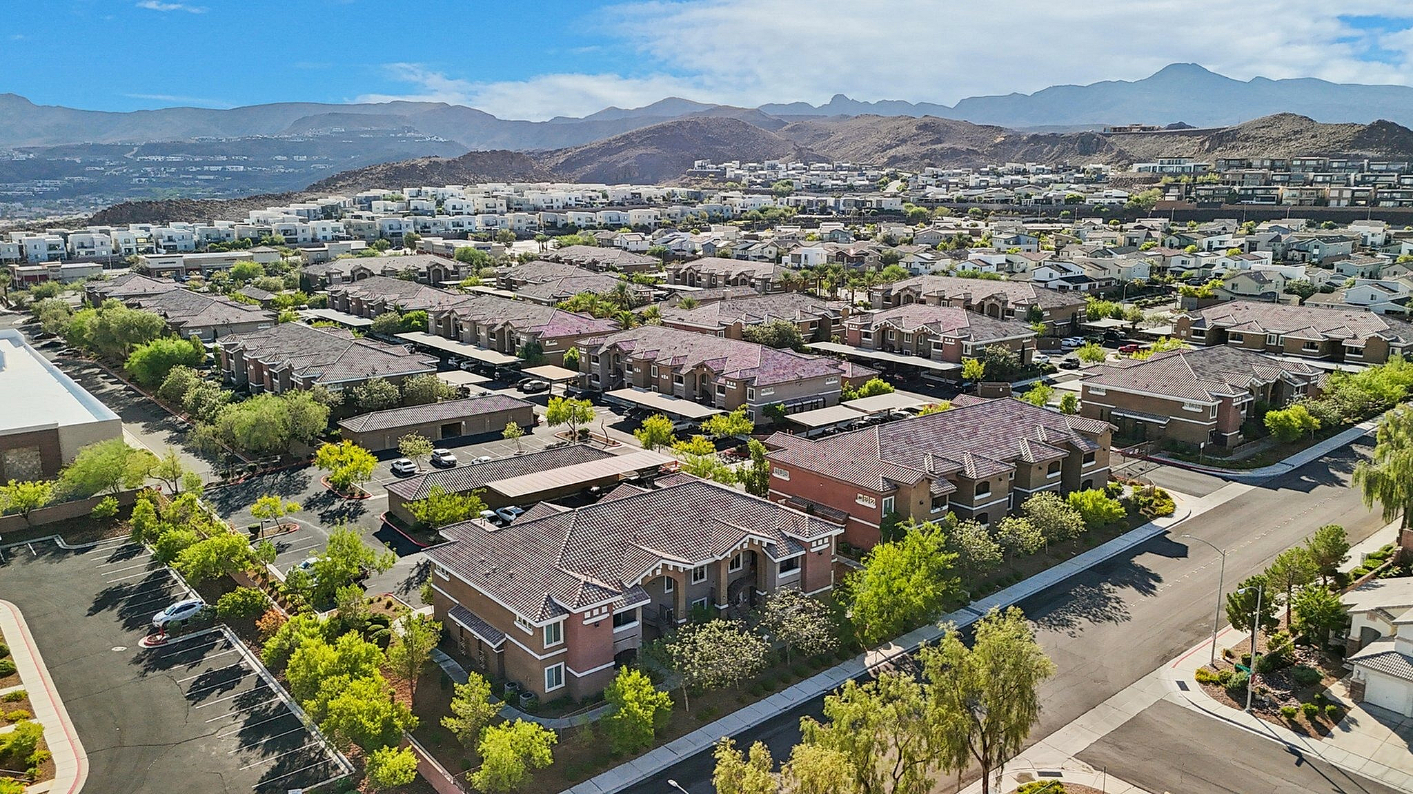 Aerial view of a picturesque suburban community nestled among scenic hills with modern townhouses, lush greenery, and well-planned streets under a clear blue sky.