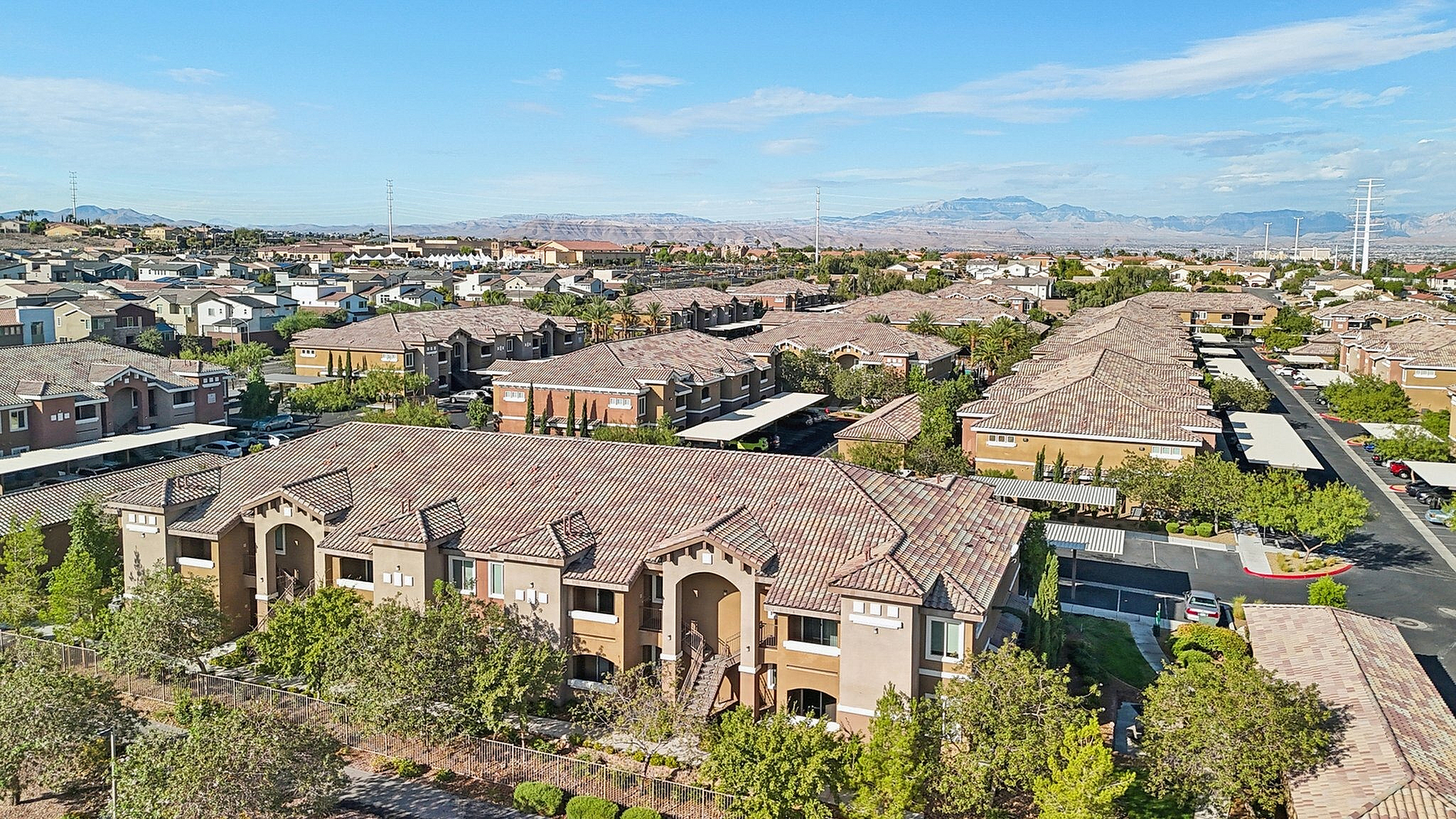 Charming aerial view of a Mediterranean-style apartment complex, showcasing beautiful tile roofing, lush greenery, and scenic mountain backdrop.