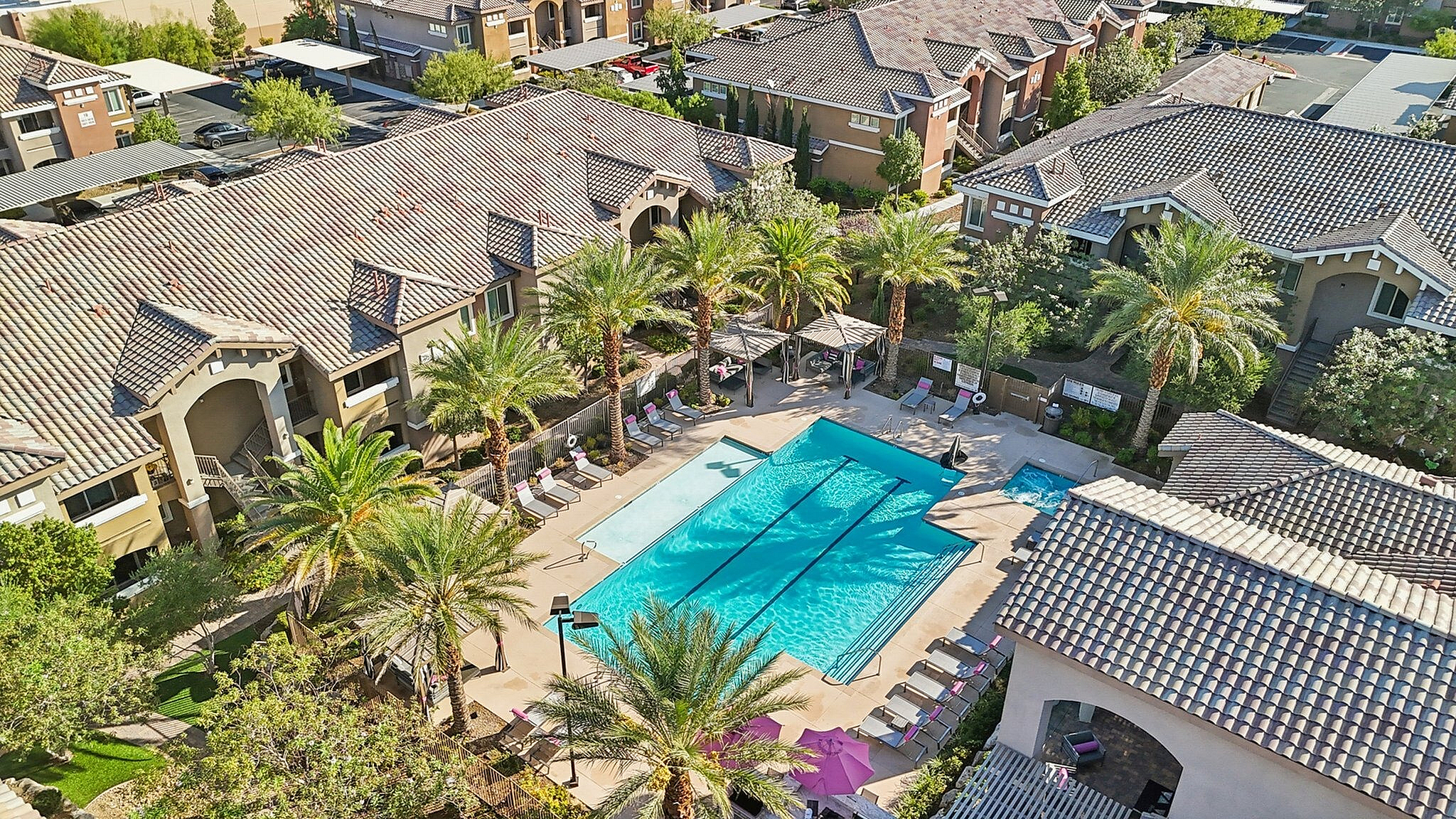 Luxurious apartment complex with tile rooftops, surrounding a stunning palm-lined swimming pool, perfect for relaxation and leisure.