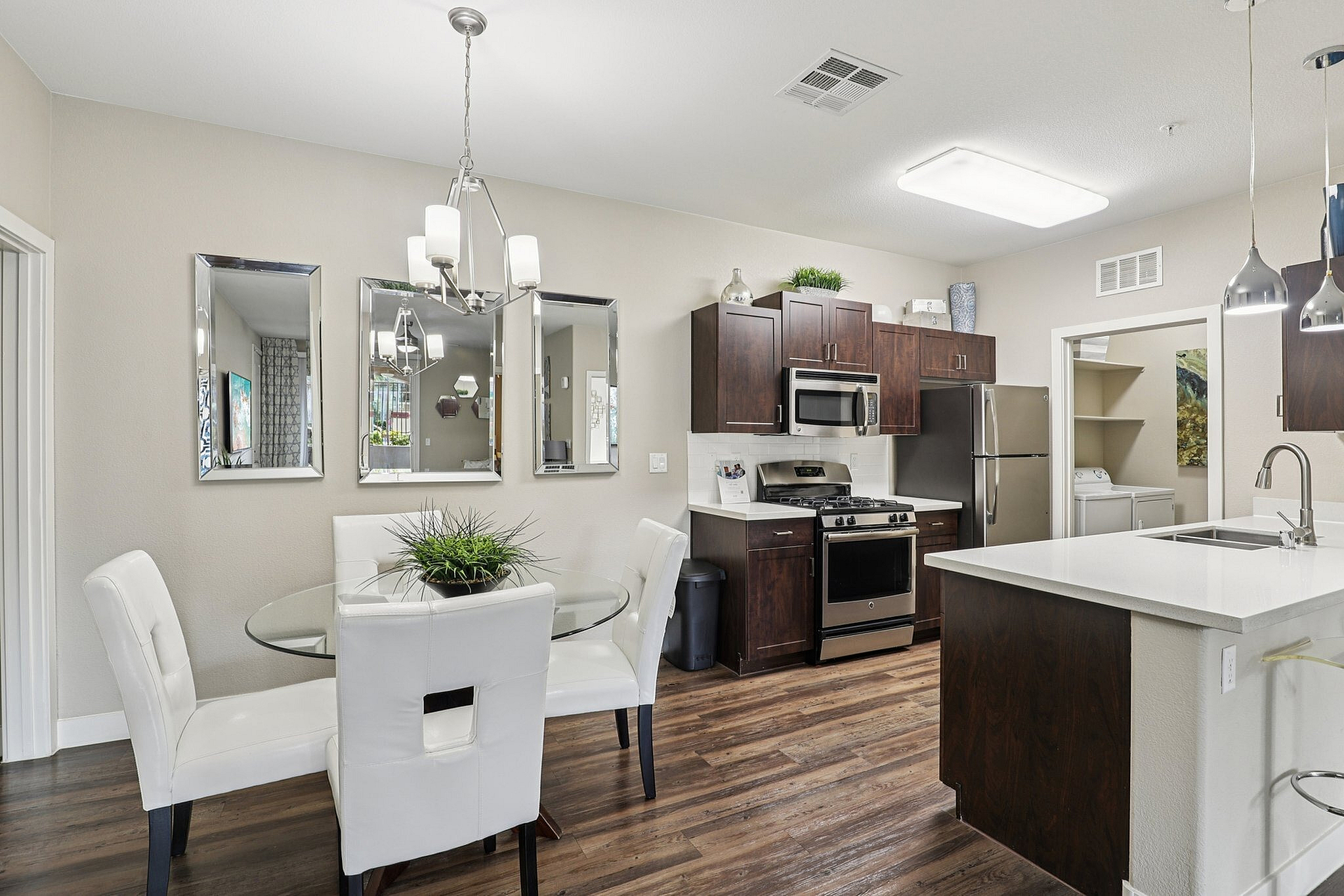 Elegant kitchen and dining area with modern appliances, white countertops, and wooden cabinetry, accompanied by a chic glass dining table with plush white chairs.