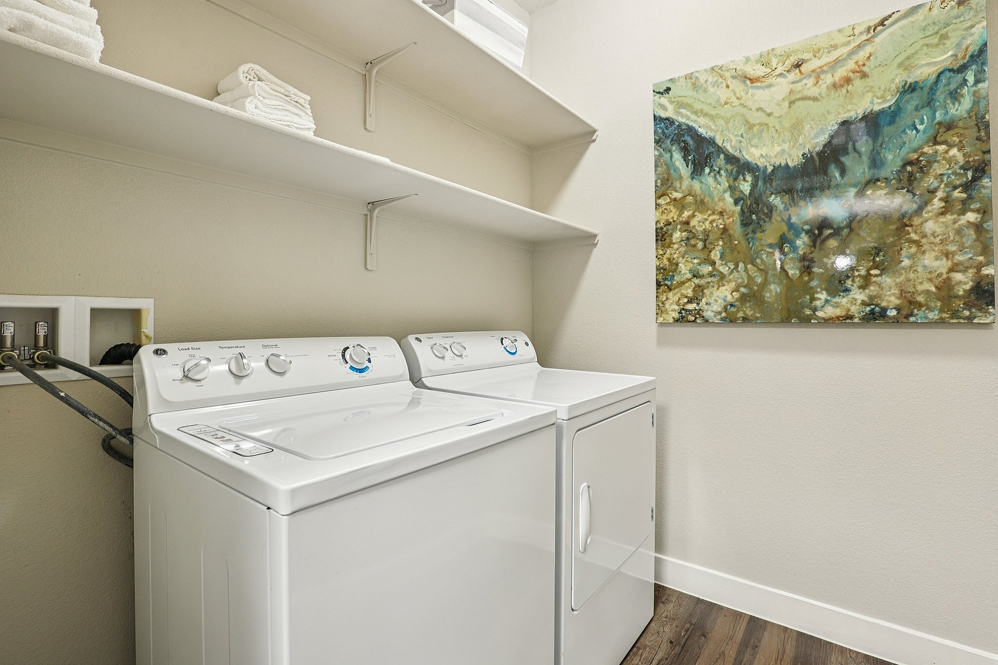 Elegant laundry room with modern washer and dryer, stylish shelving, and abstract wall art.