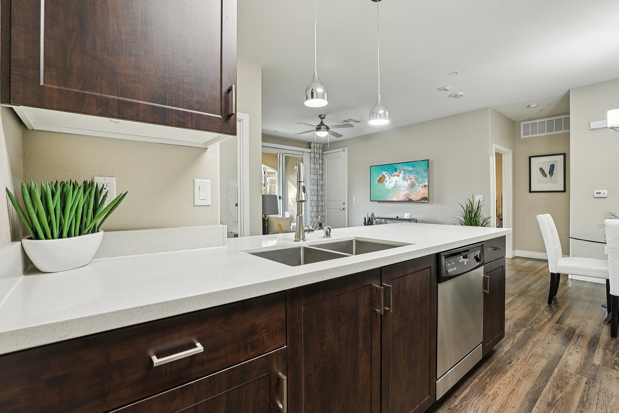 Modern open-concept kitchen with sleek countertops, pendant lighting, and rich wood cabinetry, leading to a bright living area with stylish decor.
