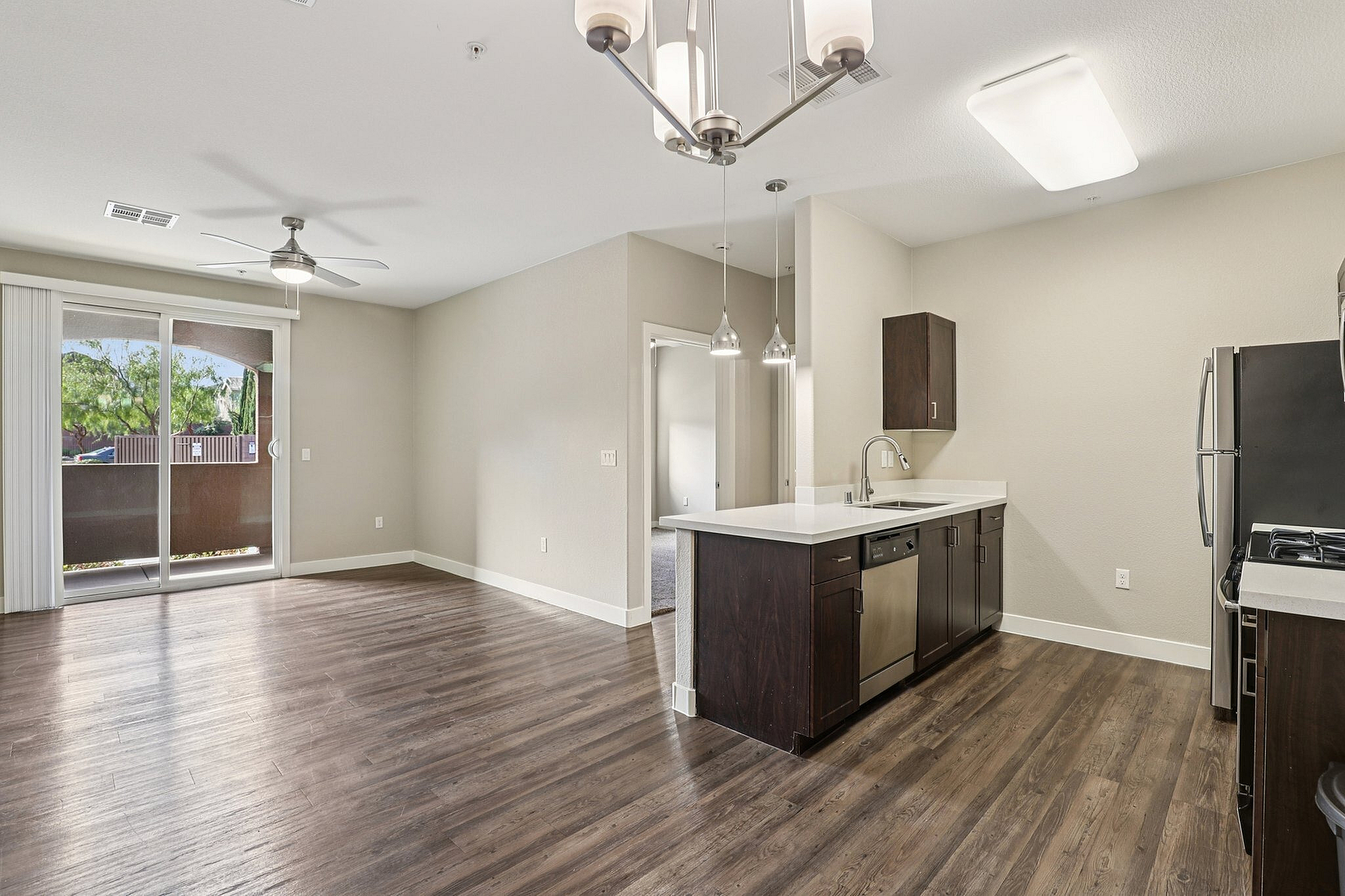 Modern open-plan living space featuring sleek hardwood floors, a contemporary kitchen with stainless steel appliances, and large glass doors leading to a balcony with lush views.
